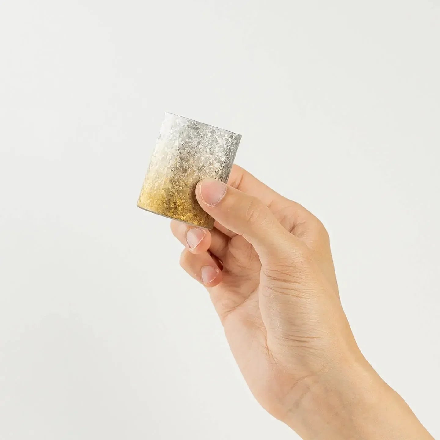 A hand holding the HORIE Titanium Sake Cup to show its side profile and crystalized finish.