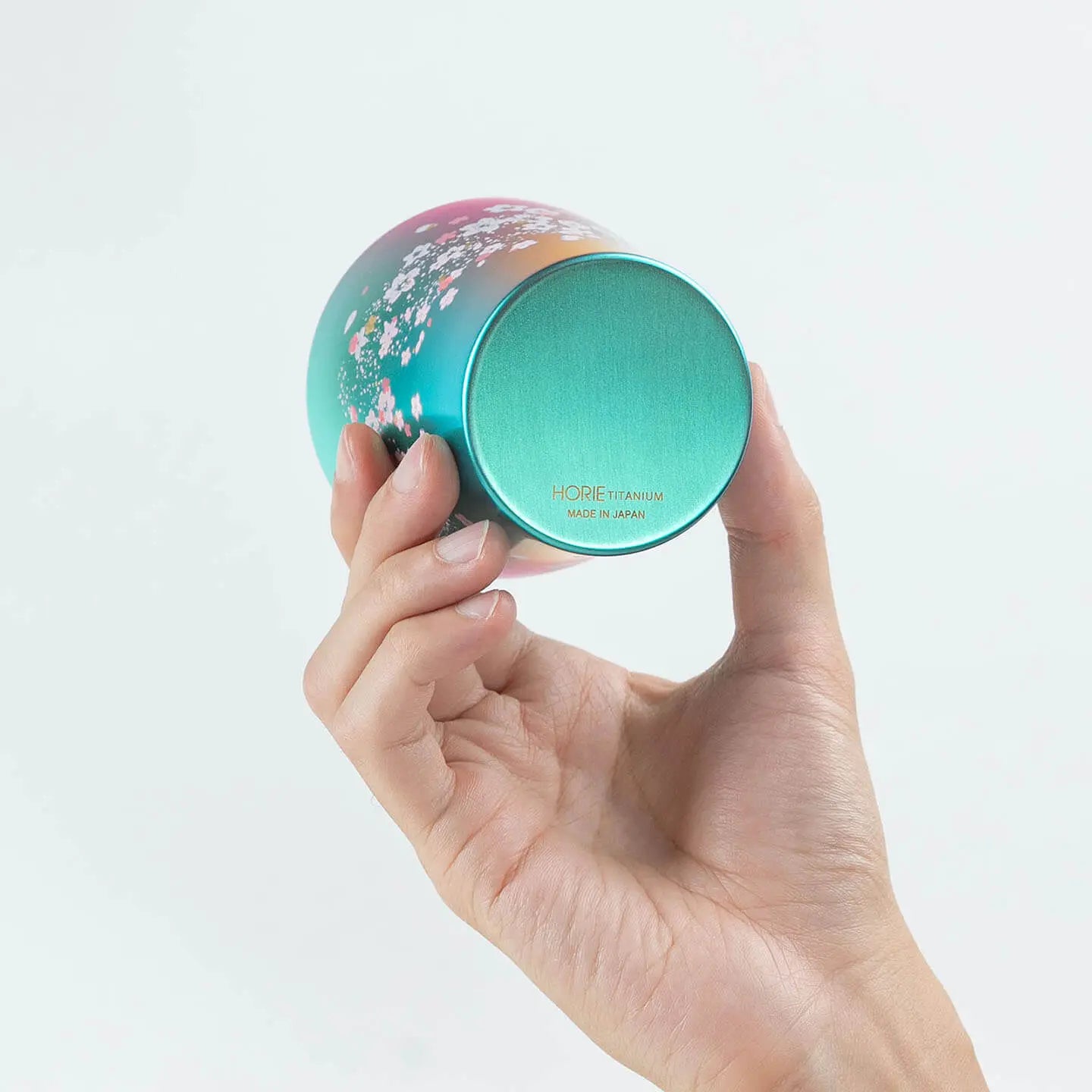 A hand holding the green HORIE tumbler to show the bottom and base detail.