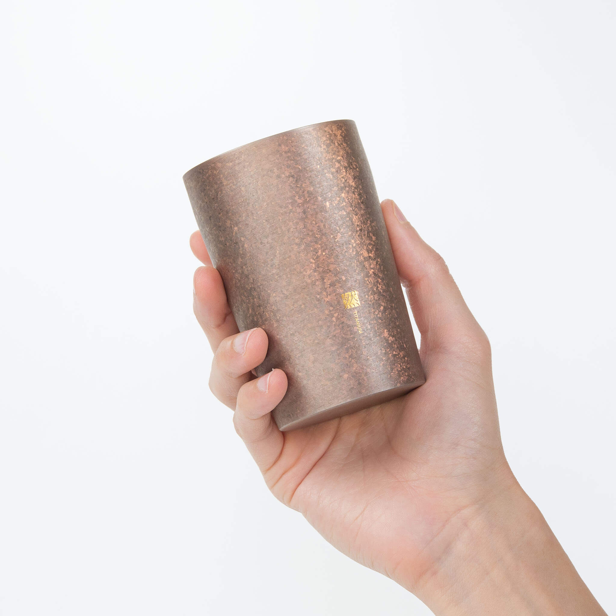 A close-up view of the Horie Zen premium titanium tumbler held in a hand, showcasing the subtle crystalline patterns of the bronze-colored metal.