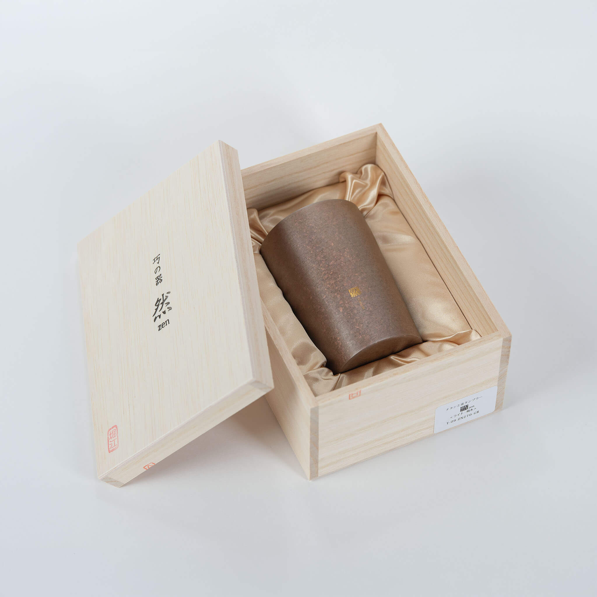 An open paulownia wooden box revealing the Horie Zen 270ml titanium tumbler resting on a luxury gold silk lining.