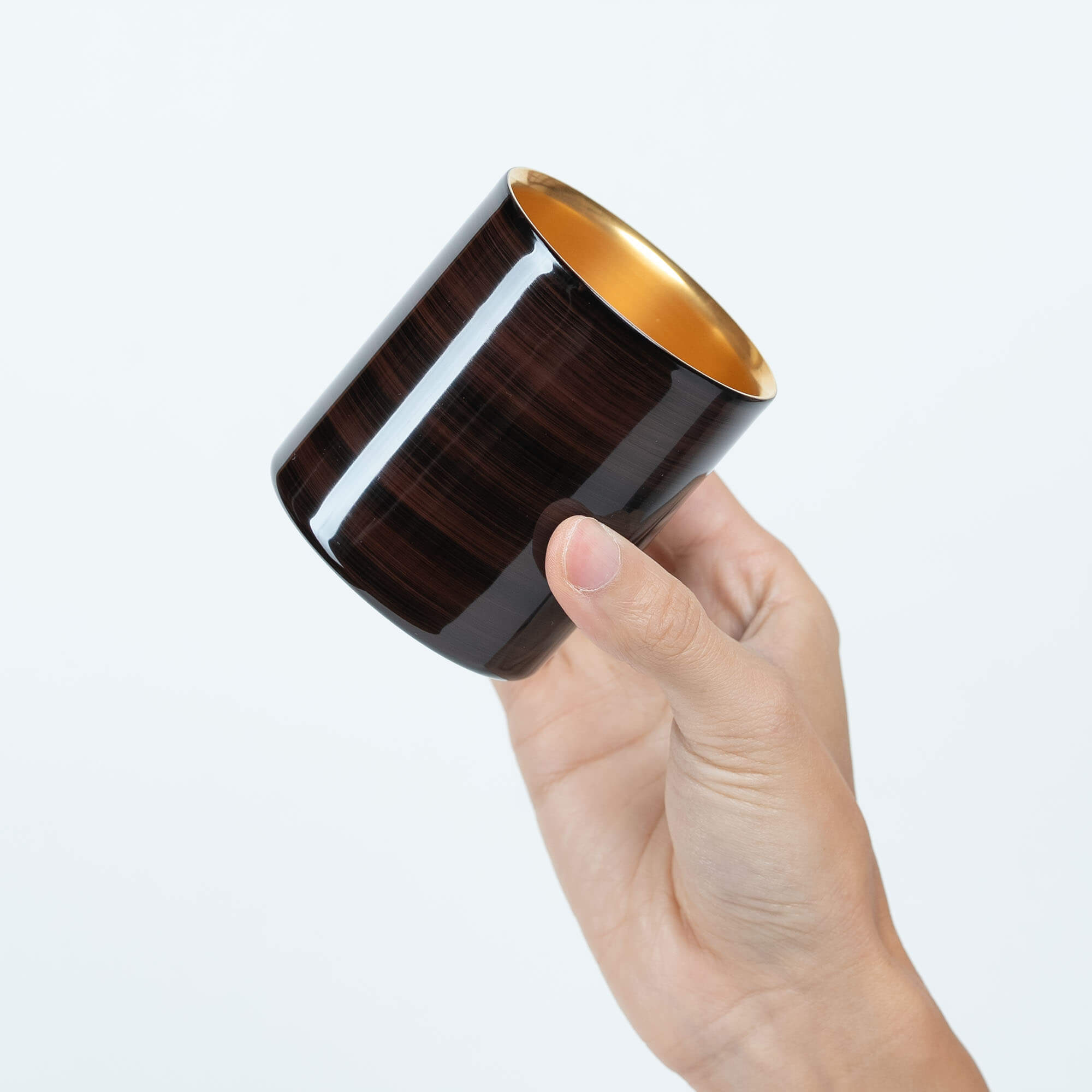 Handheld brown lacquered sake cup showing its reflective gold-plated interior