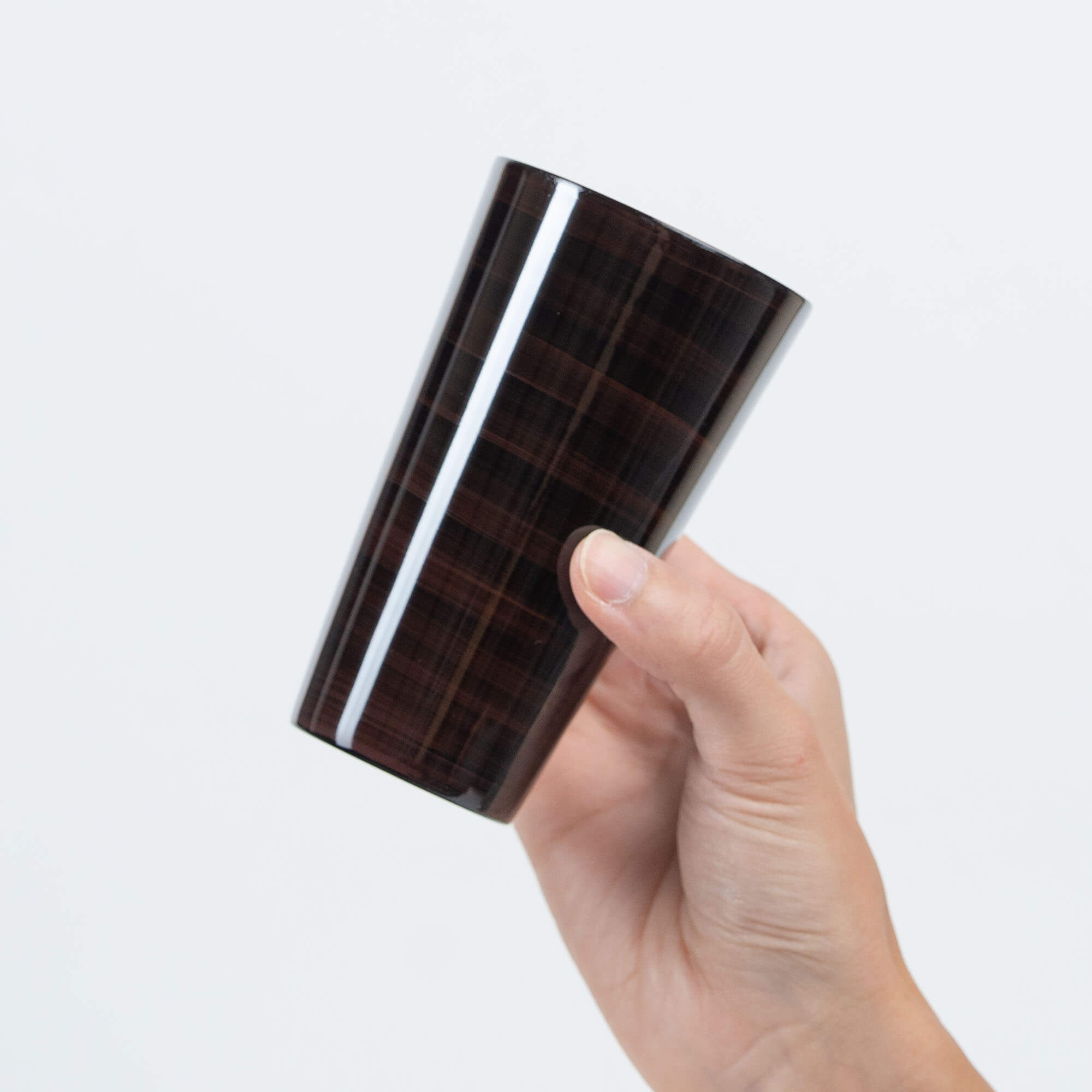 Side view of a brown Japanese lacquered stainless steel tumbler held in one hand