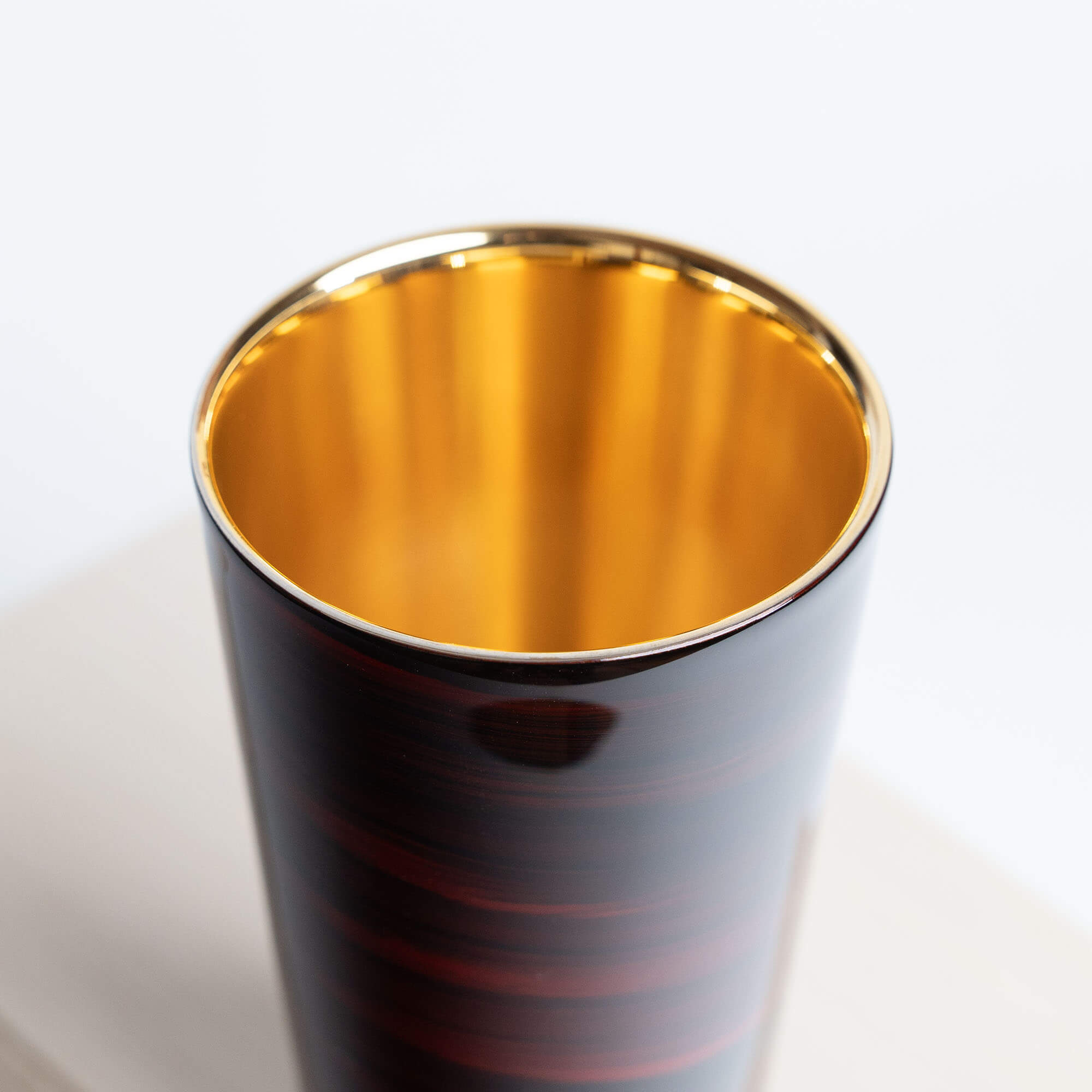 Angled view of a red lacquered stainless steel tumbler with a gold-plated interior