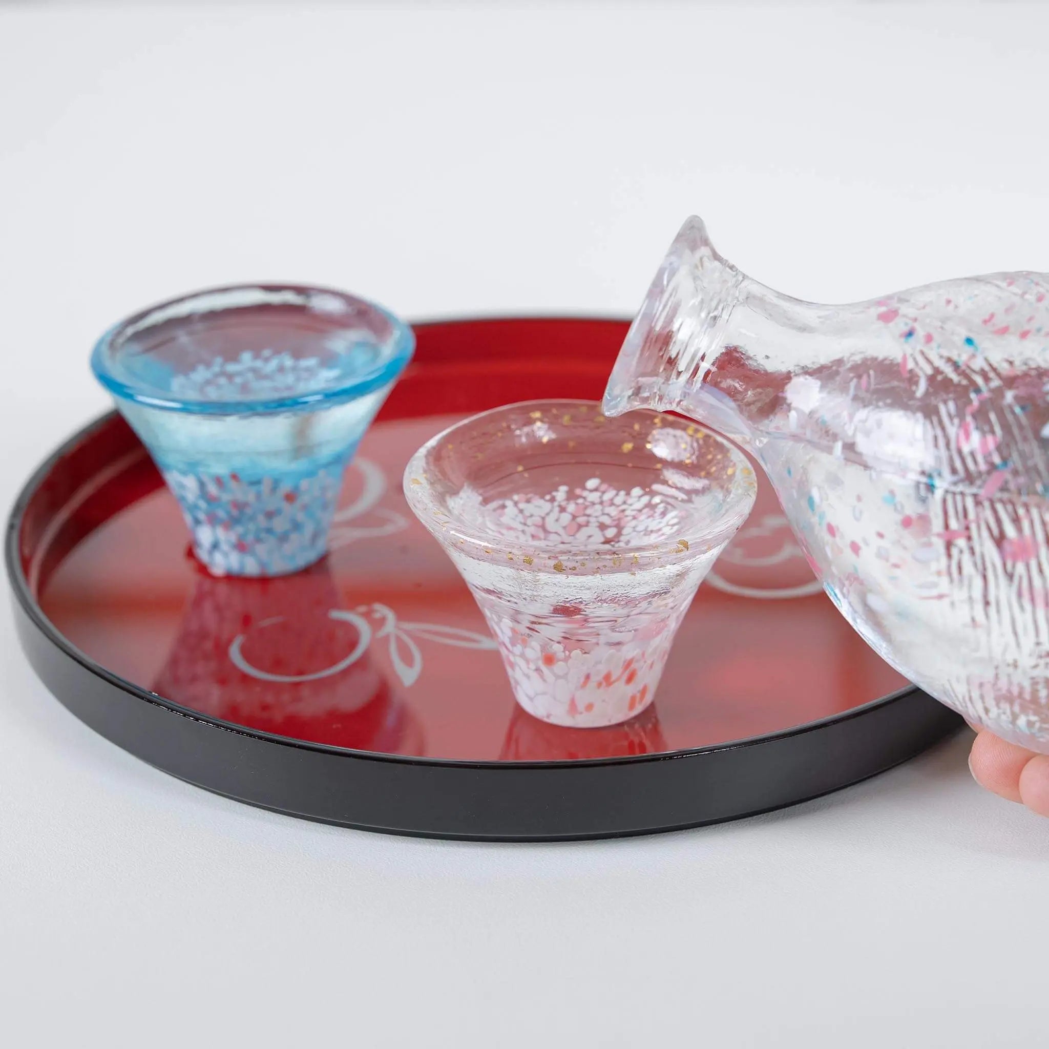 Pouring sake into handmade Japanese glass cup from sakura and Mount Fuji sake bottle.