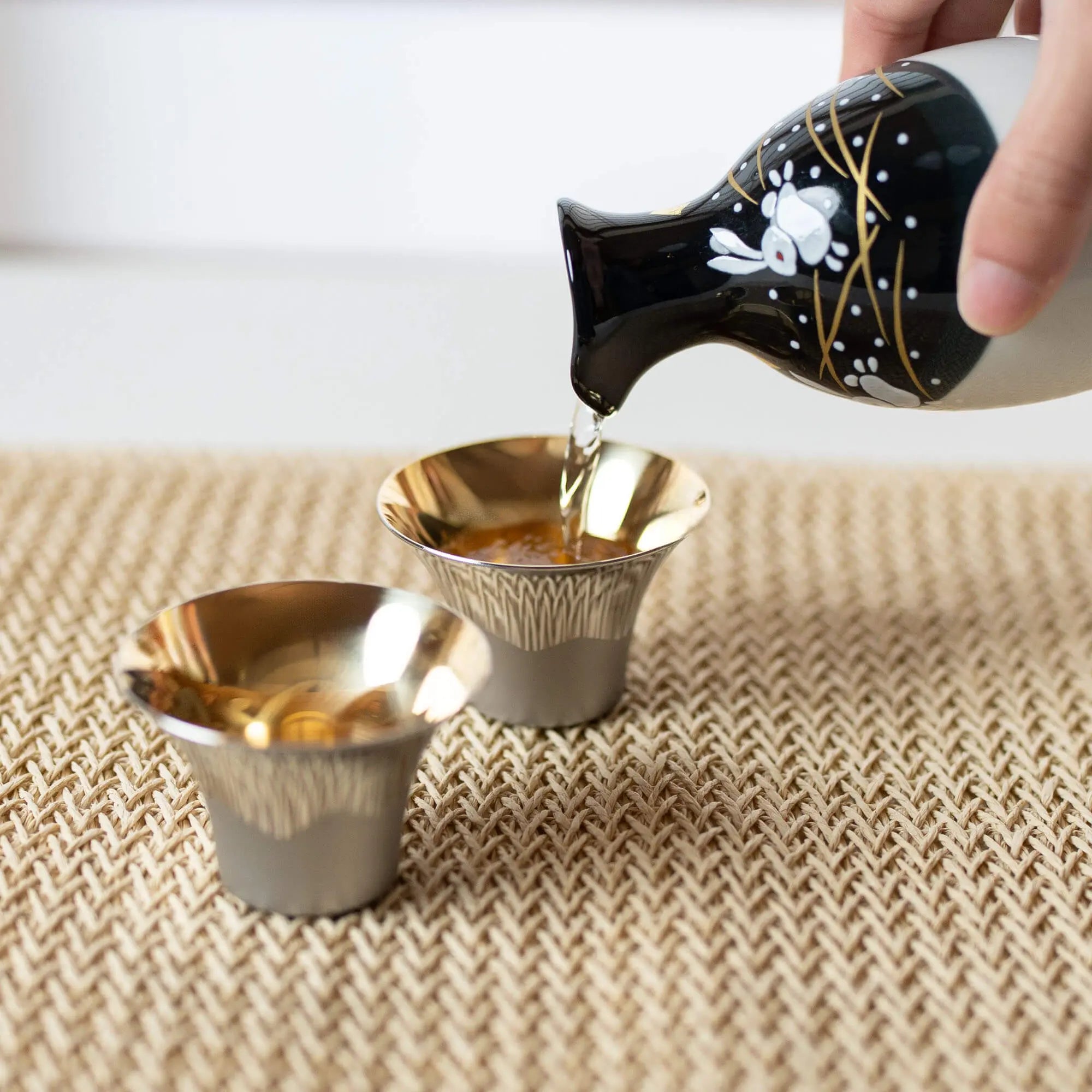 Pouring sake into Japanese Fuji-design stainless steel sake cup
