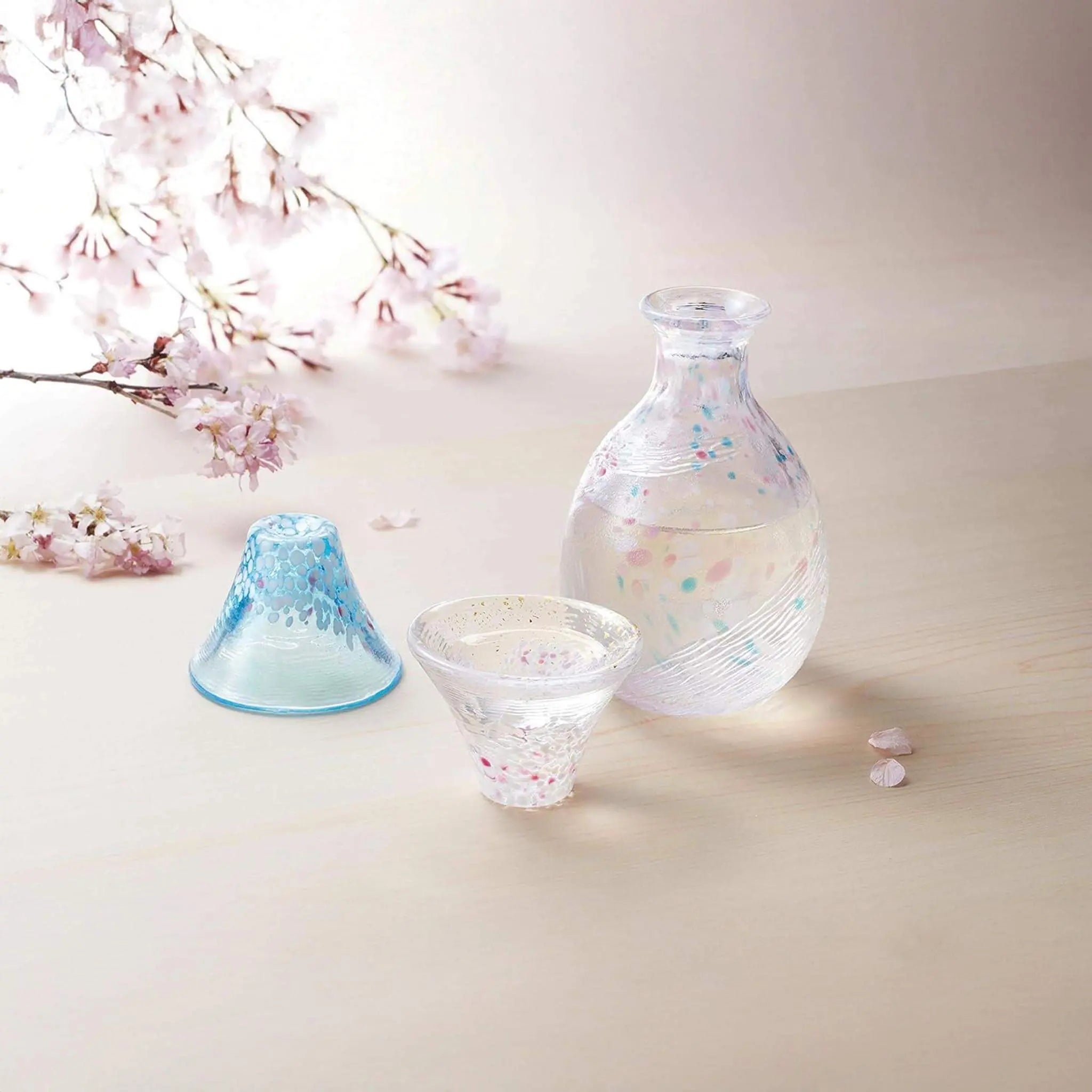 Japanese sake set with cherry blossom and Mount Fuji design, handmade glass cups and bottle displayed in spring sakura scene.