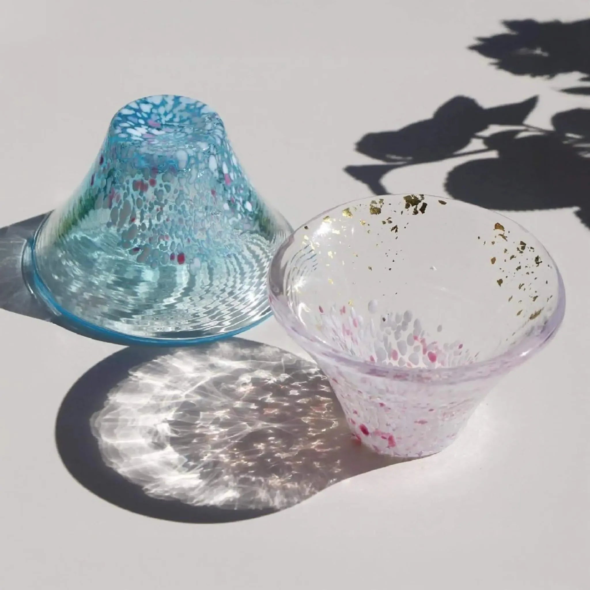 Handmade Japanese sake cups inspired by cherry blossoms and Mount Fuji, delicate glass texture with beautiful light reflections.