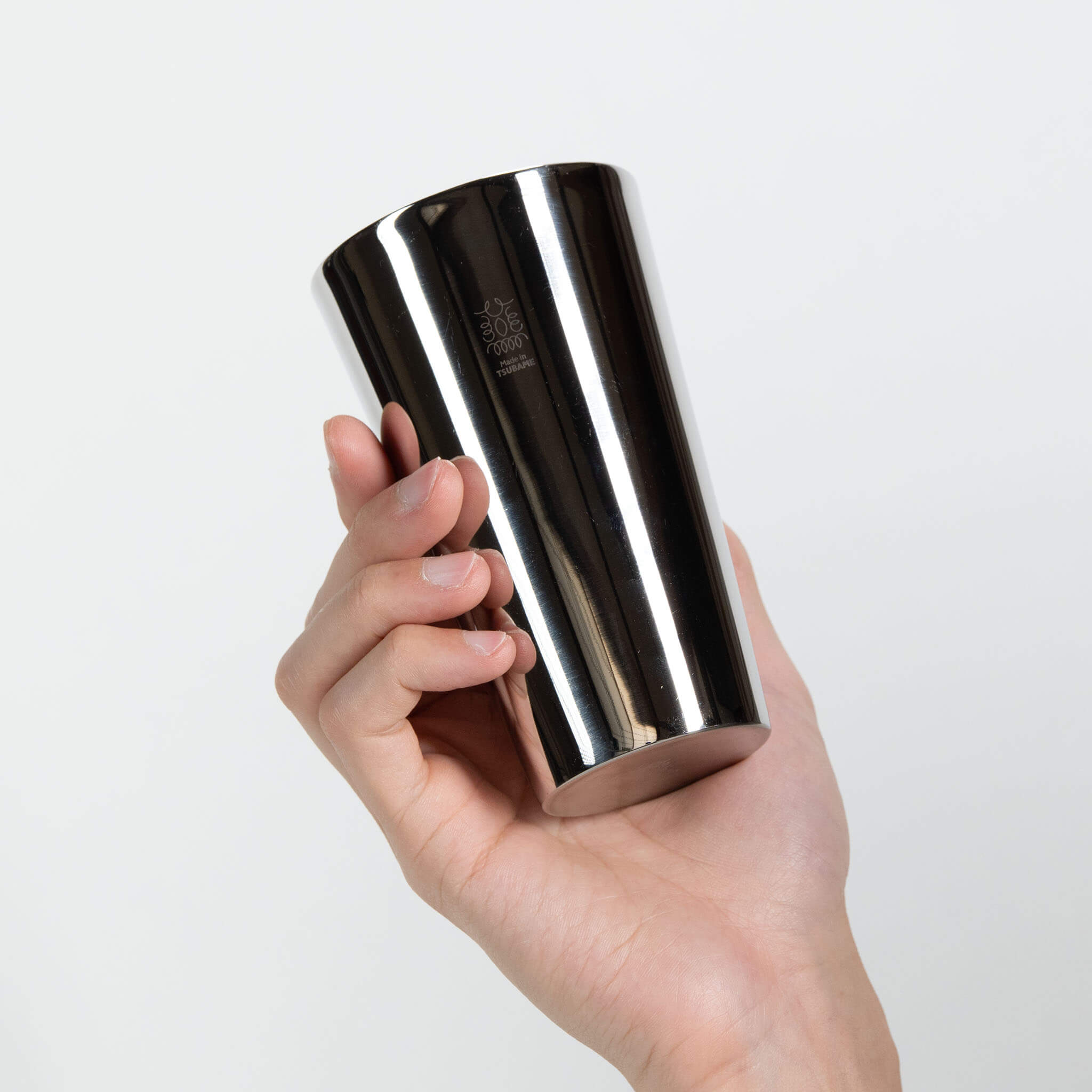 Side profile of the silver polished stainless steel whisky tumbler held smoothly in hand.