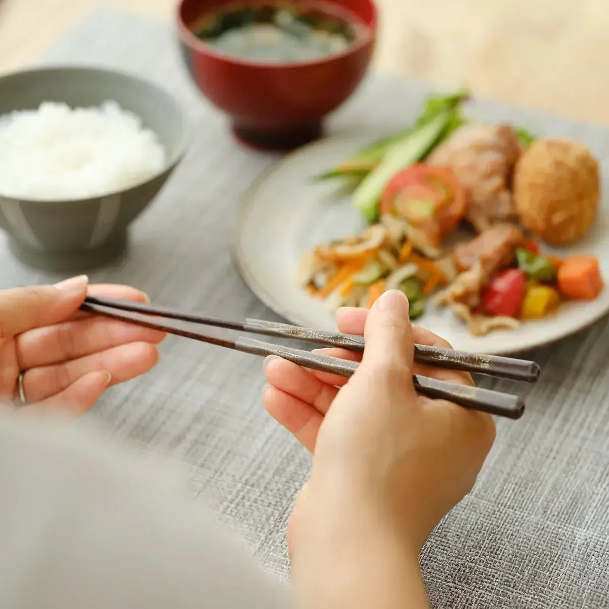 Hand holding a Wakasa lacquer chopstick, highlighting its smooth lacquer finish and ergonomic design.