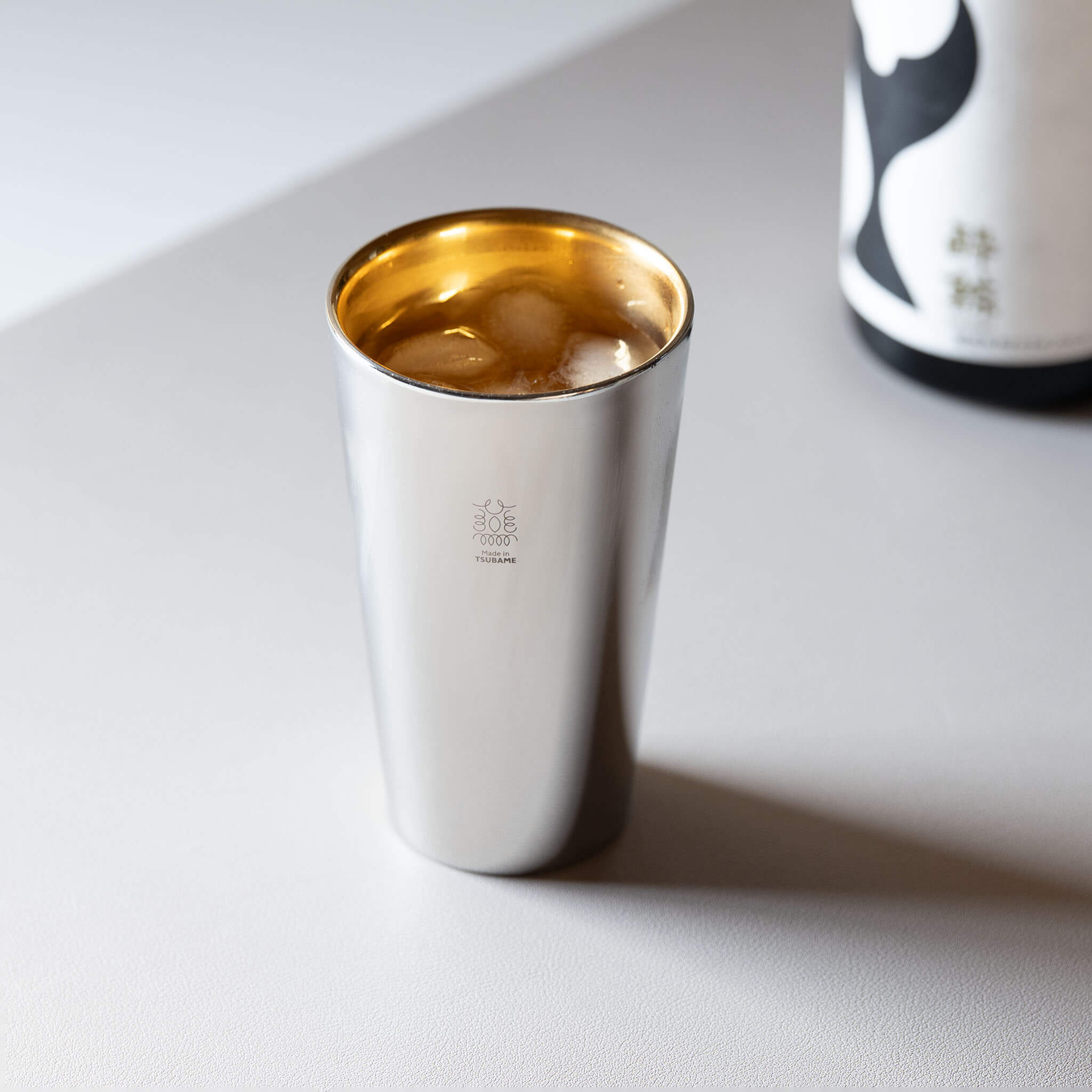 Premium Made in Tsubame 18-8 stainless steel sake tumbler served with ice next to a sake bottle.