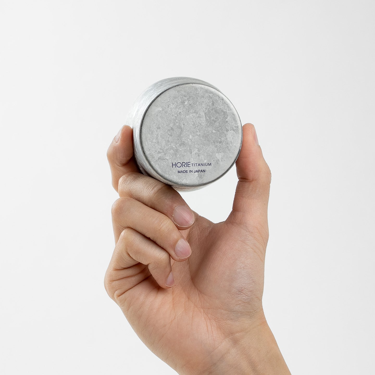 Hand holding HORIE Kamazukuri 270ml Silver Titanium Tumbler upside down, white background