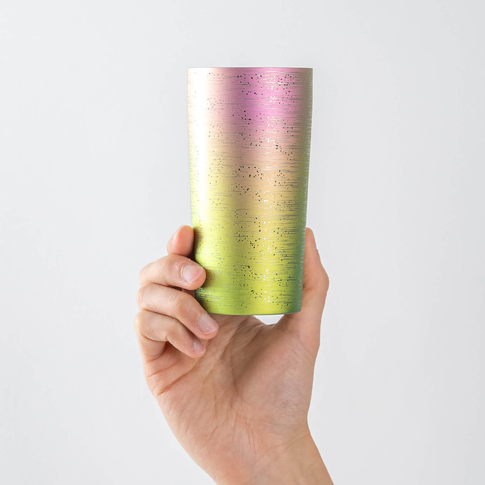 Hand holding HORIE Ryo titanium tumbler with pink-yellow-green gradient finish, ideal for pouring beer with a smooth, creamy head