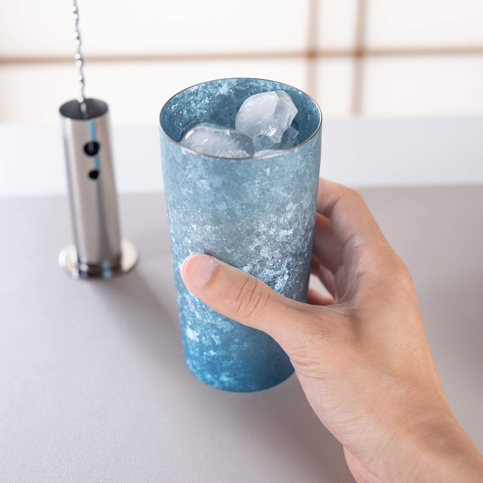 HORIE Titanium Kamazukuri 350ml Blue Tumbler held in hand filled with ice cubes, side view showing frost-like texture