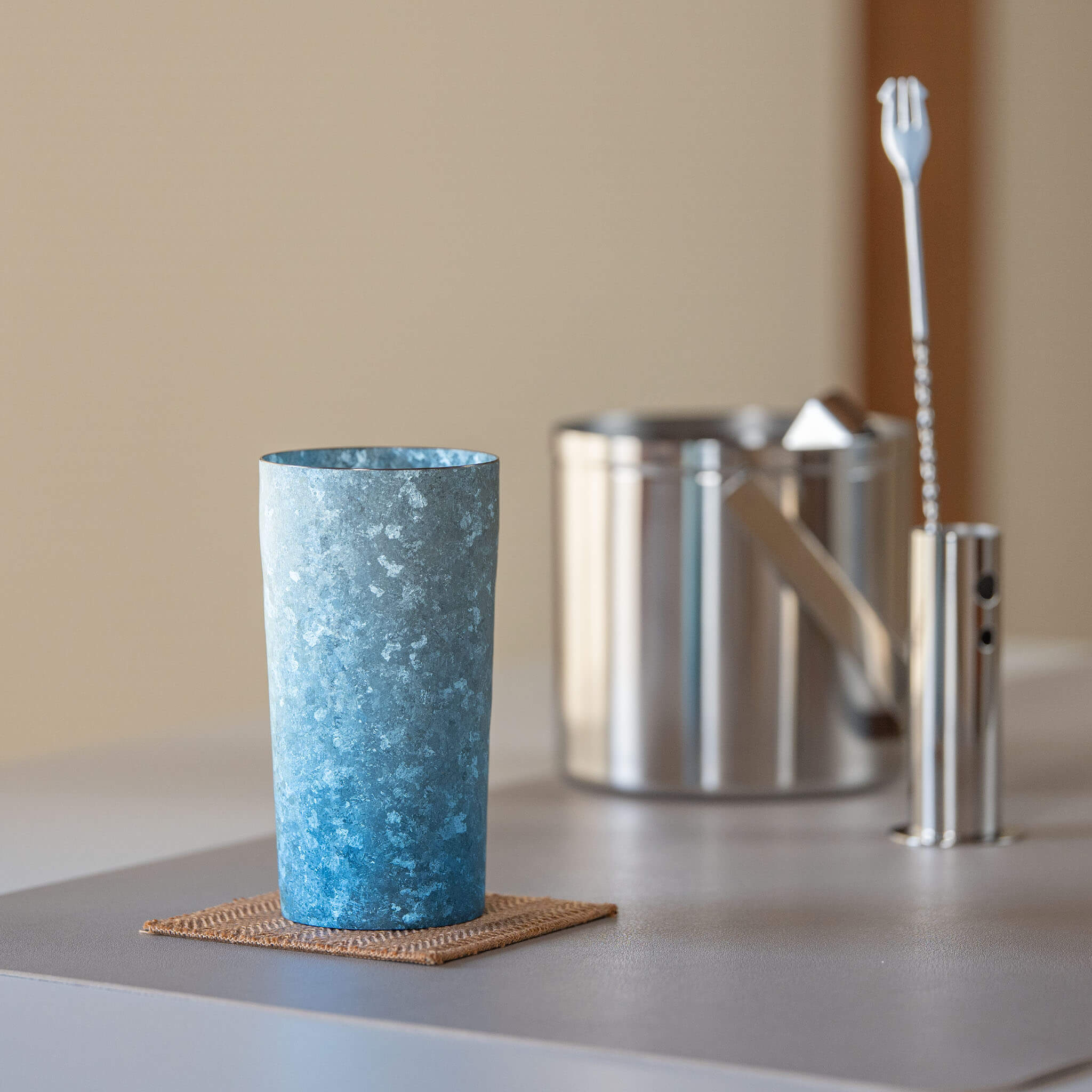 HORIE Titanium Kamazukuri 350ml Blue Tumbler on woven coaster with bar spoon, warm ambient bar setting