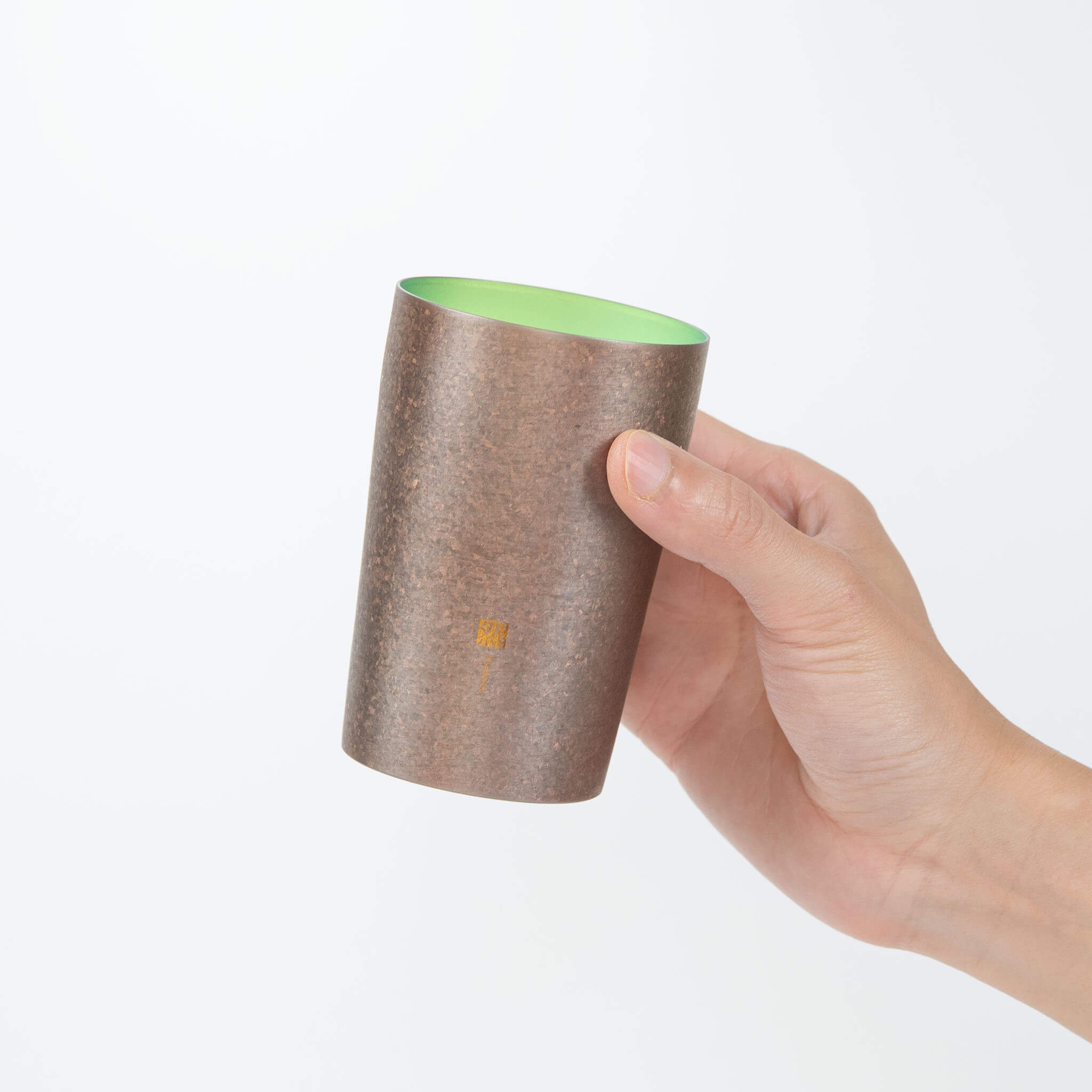 A hand holding the Horie Zen 270ml titanium tumbler against a white background, highlighting its ergonomic shape and rustic bronze finish.