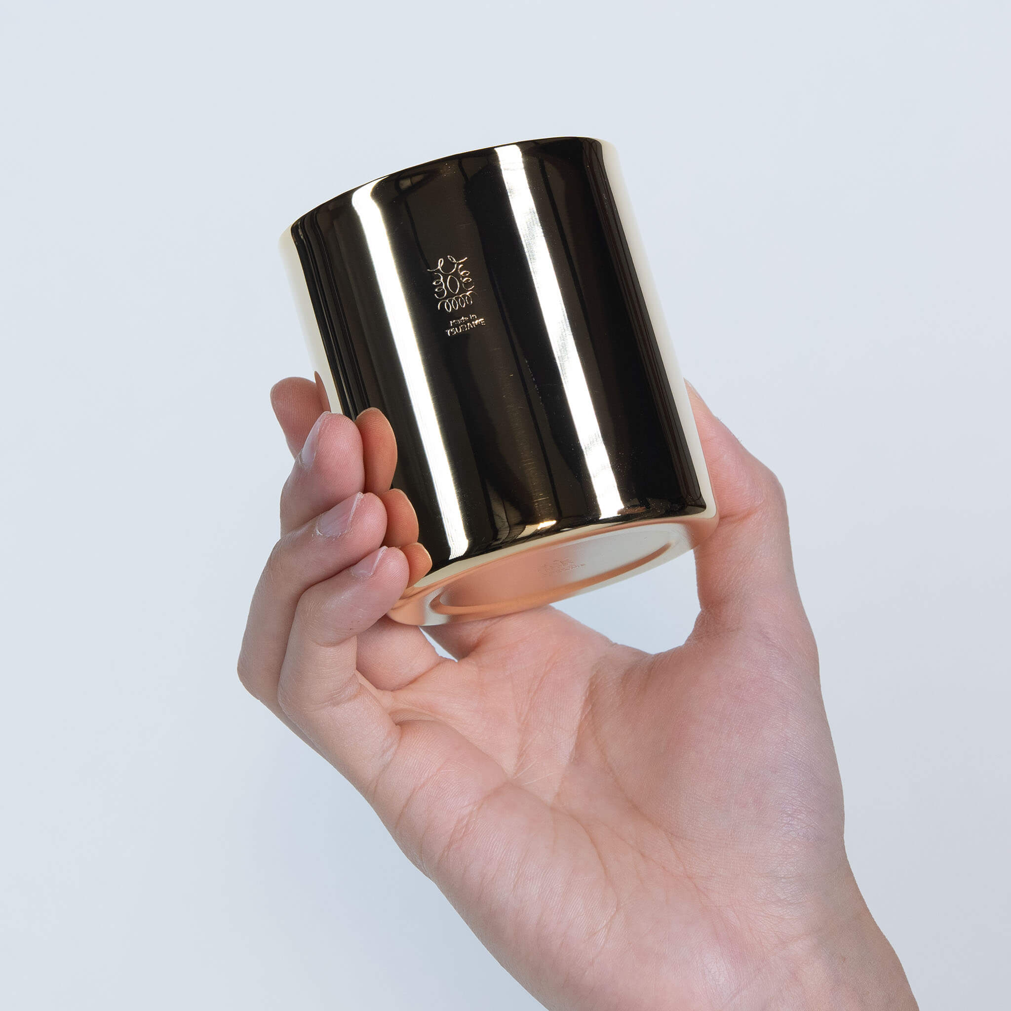 Side view of the handcrafted Japanese gold cup held gently to display its flawless metallic reflection for tea or juice.