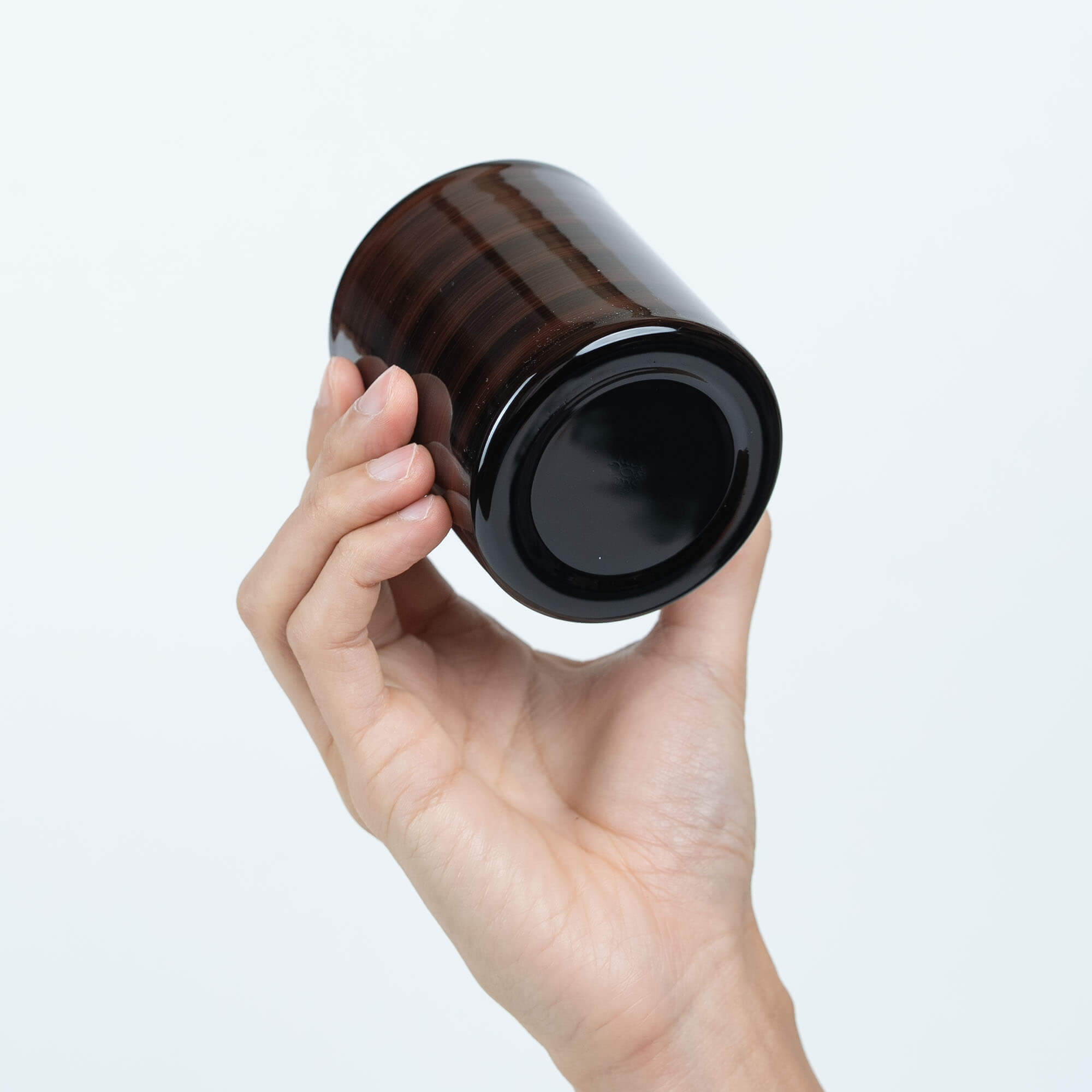 Base view of a brown Japanese lacquered stainless steel sake cup held in one hand
