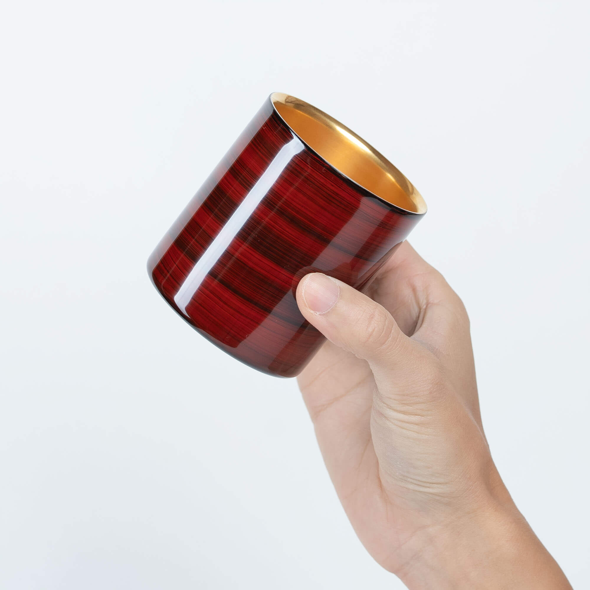 Hand holding a red Japanese lacquered sake cup at a side angle