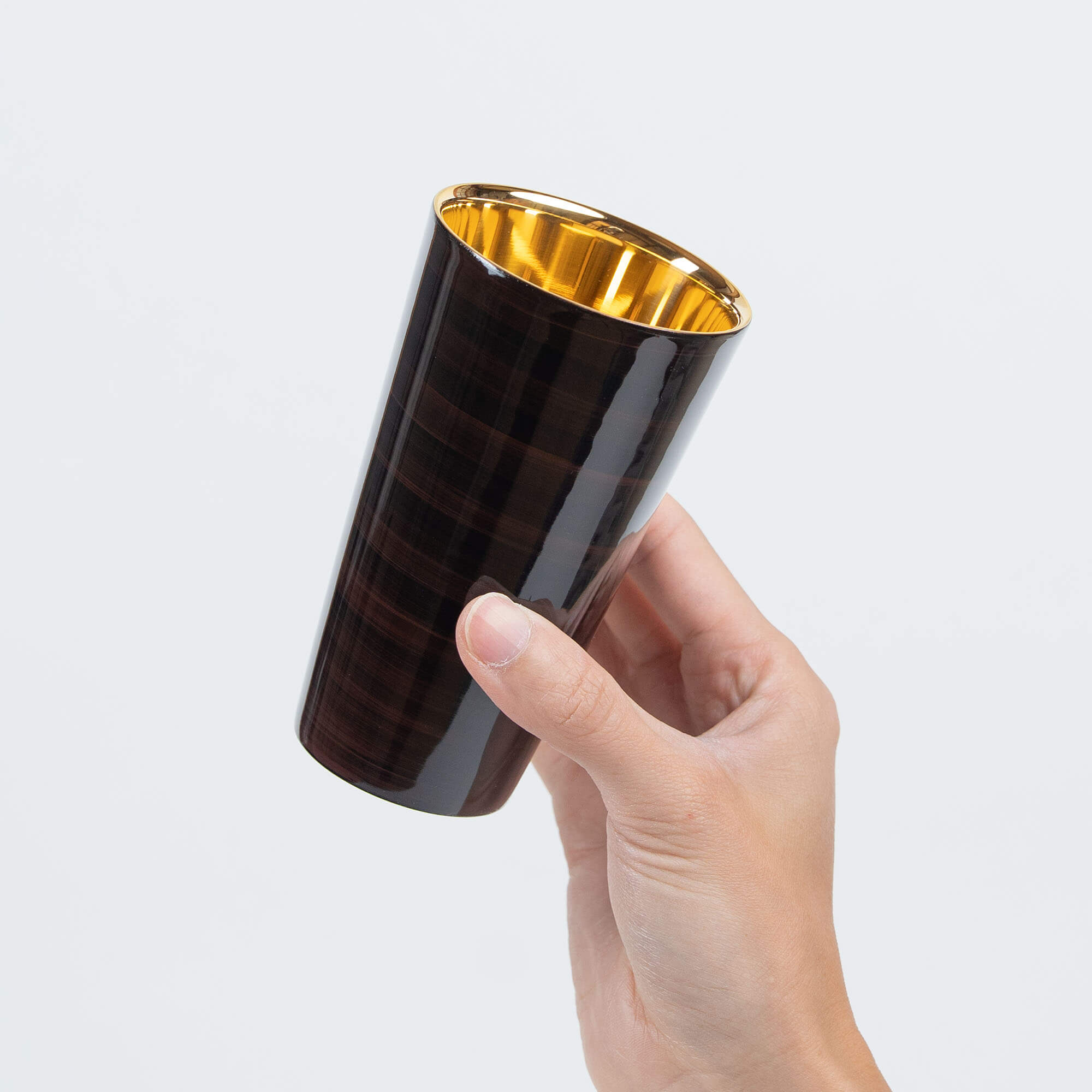 Handheld brown lacquered tumbler showing its gold-plated interior