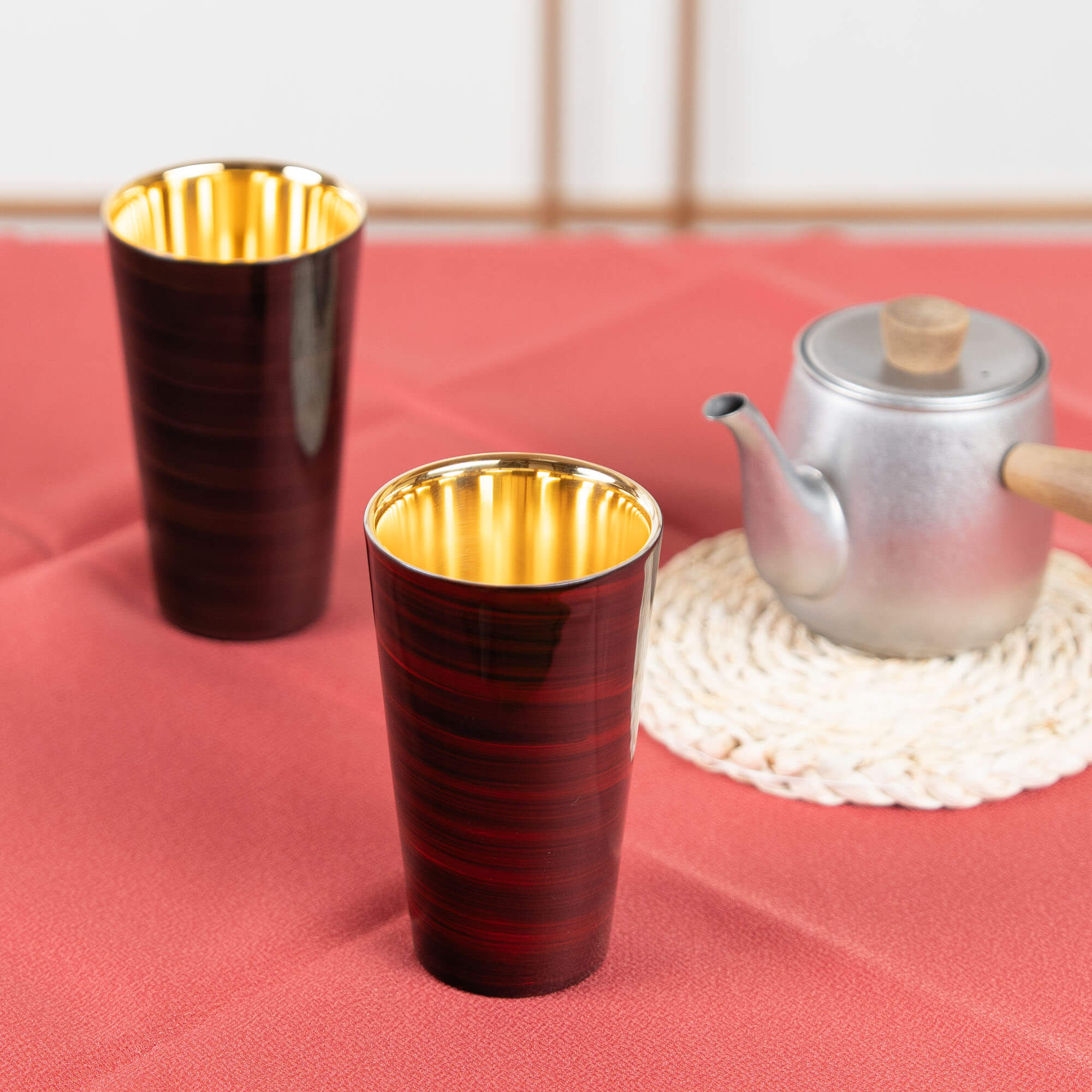 Red and brown Japanese lacquered tumblers arranged with a teapot on a red table