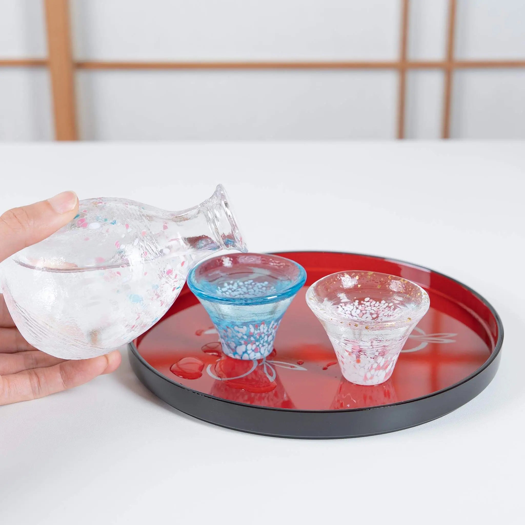 Serving scene of Japanese sake set with sakura and Mount Fuji motif, handmade glass cups and bottle.