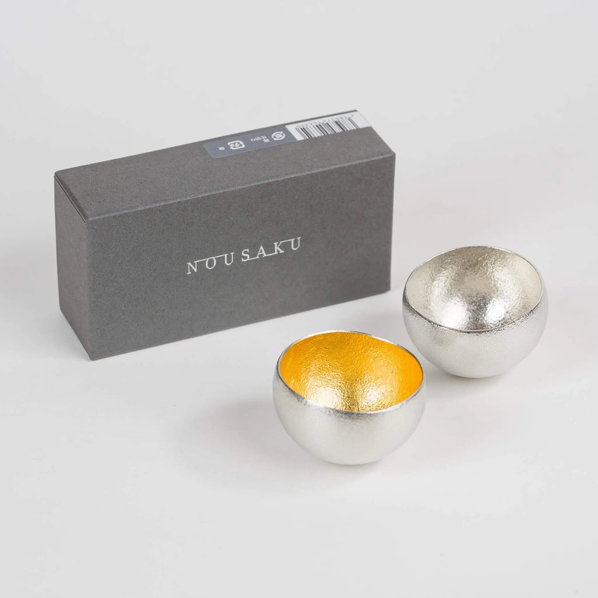 Nousaku rocking sake cup set with gold and silver finishes next to its premium gift box.