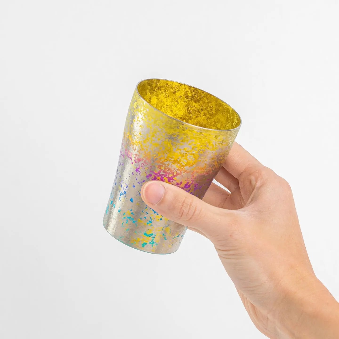 Hand holding the titanium tumbler at an angle, showing the golden yellow interior and rainbow exterior.