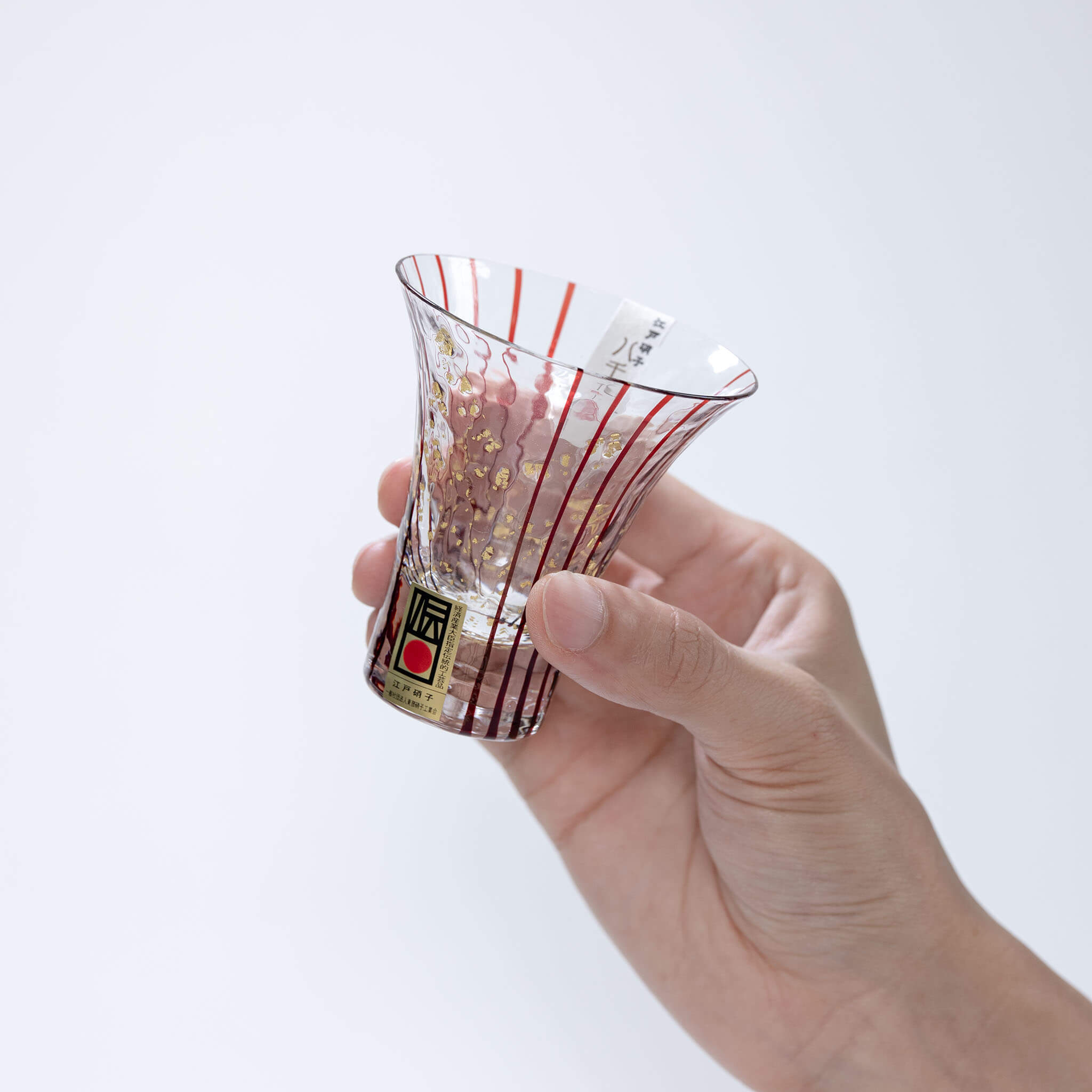 Side view of a hand holding the red-striped Hanamizake sake glass