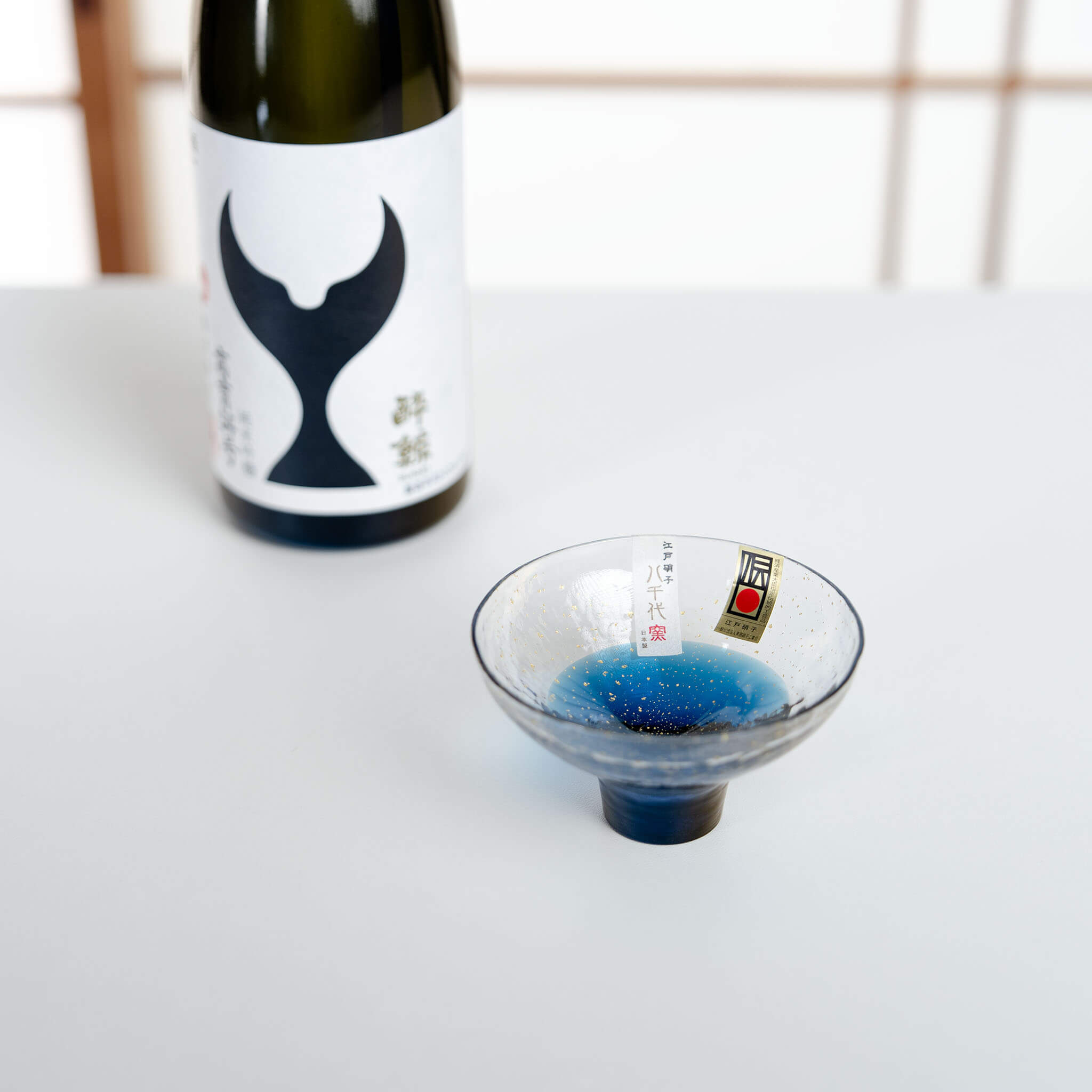 Yachiyo Kiln handblown sake cup displayed beside a Japanese sake bottle