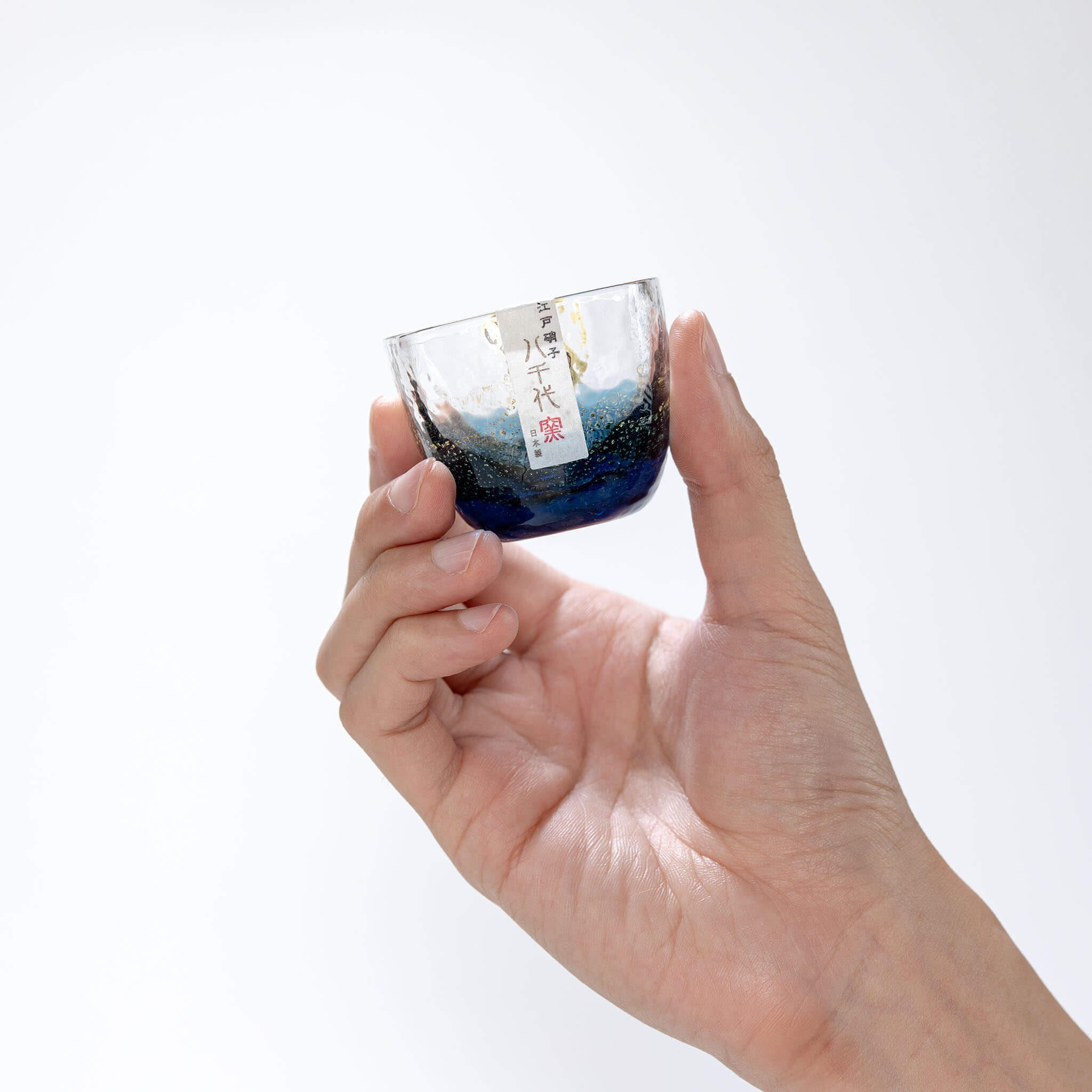 Side view of a hand holding the blue Yachiyo Kiln sake cup