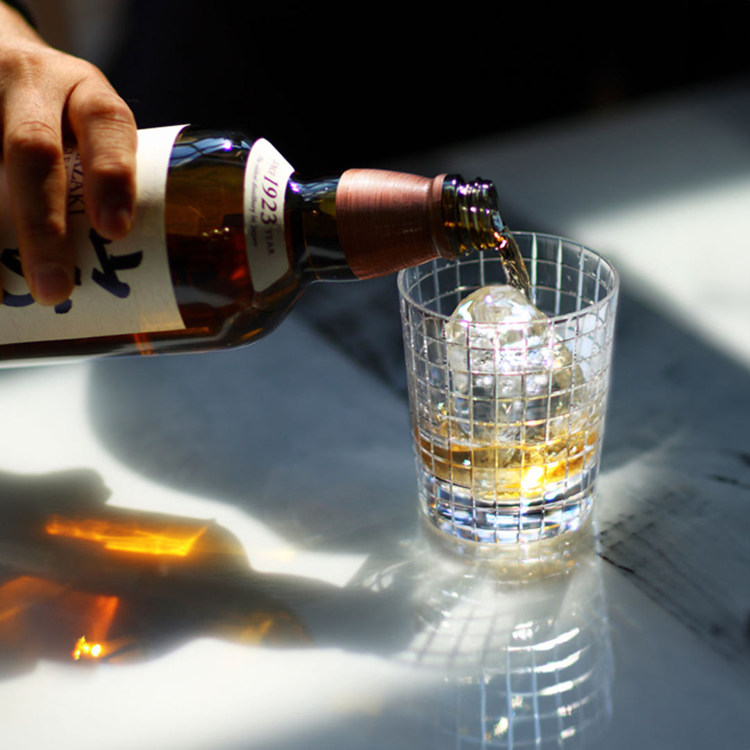 Pouring whiskey into Yamazaki × Takeo Kikuchi crystal rock glass, showcasing the interaction between the whiskey and the finely cut crystal glass.